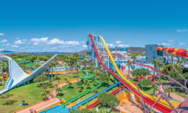 Aerial view of Aquashow Park Hotel in Quarteira, Algarve, showing the hotel buildings, outdoor pools, water park attractions, and surrounding lush greenery under clear blue skies.