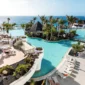 Cenário tropical do Hotel Club Jandia Princess, com a área da piscina rodeada de palmeiras e vistas para o oceano