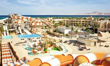 Aerial view of Coral Sea Water World resort showing colourful water slides, swimming pools, lush gardens, and beachfront in Sharm El Sheikh.