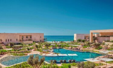 Fairmont Taghazout Bay exterior with sea view, infinity pools and sun loungers under palm trees