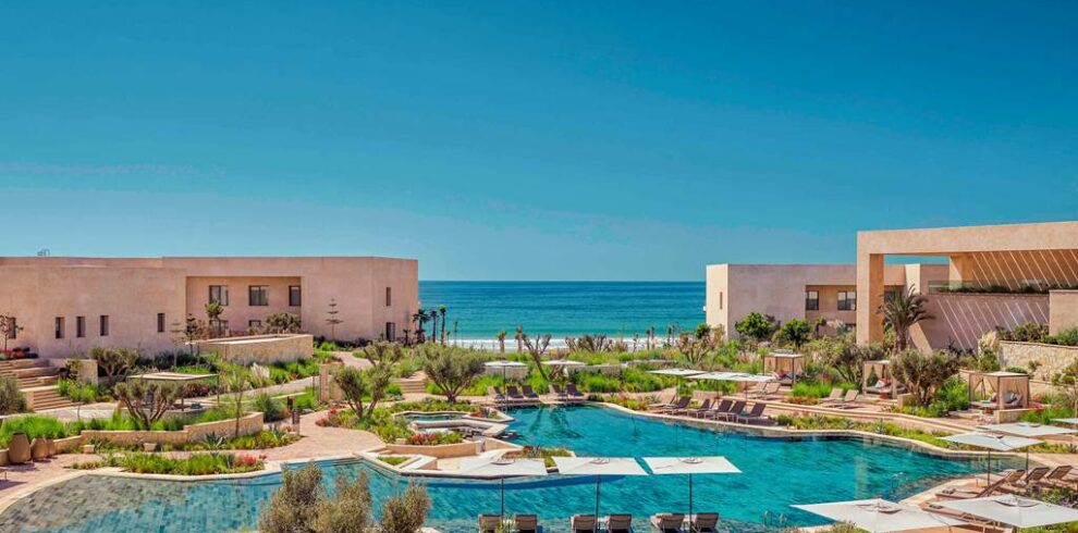 Fairmont Taghazout Bay exterior with sea view, infinity pools and sun loungers under palm trees