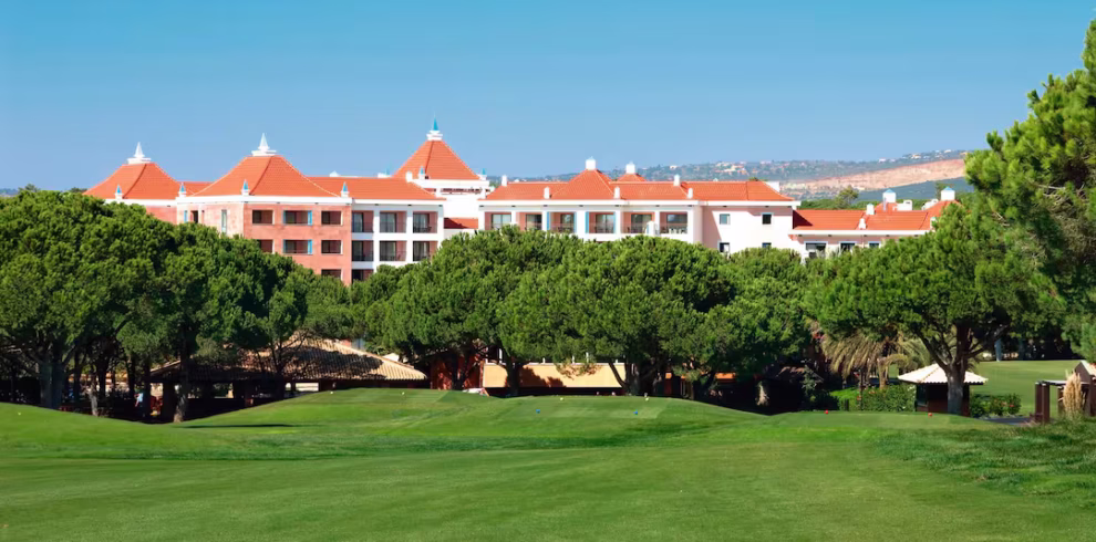 View of Hilton Vilamoura As Cascatas Golf Resort & Spa with manicured green lawns, pine trees, and elegant Mediterranean-style architecture.